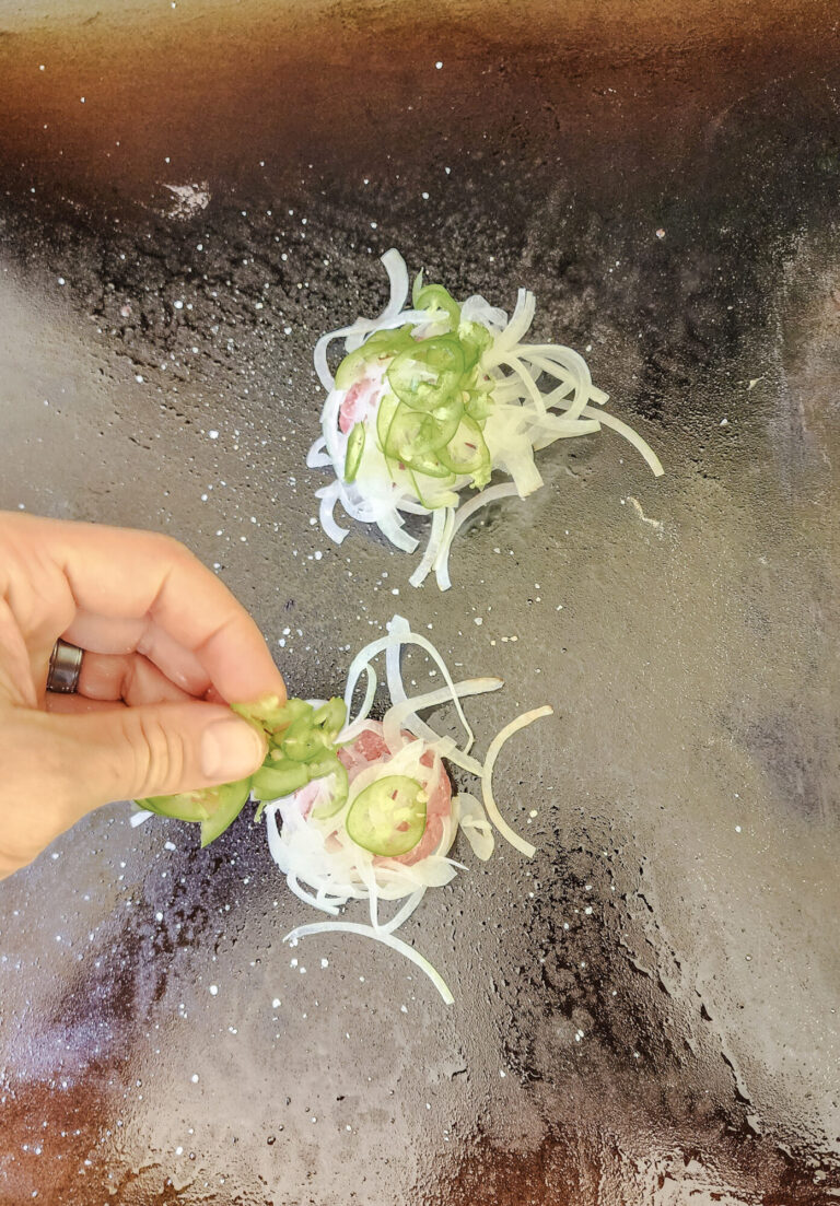 Adding shaved onions and jalapenos to burger patties