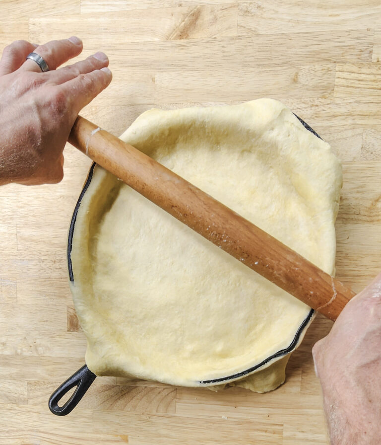 Cutting the excess crust off with the rolling pin.