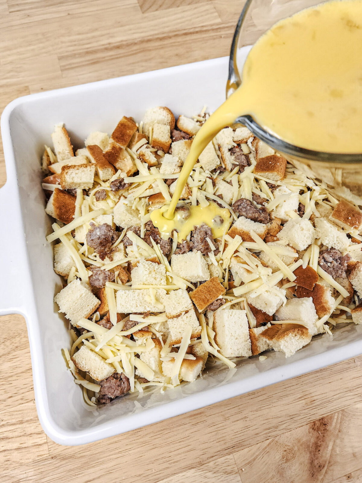 Pouring the egg mixture over the bread cubes, sausage, and cheese.