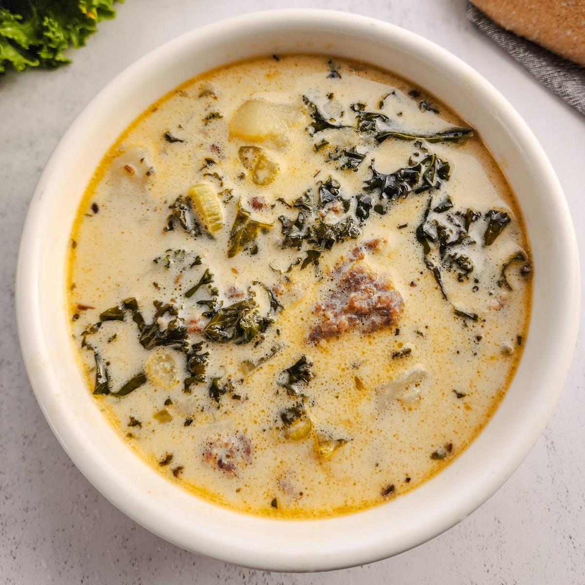 A white bowl of Rustic Zuppa Toscana with italian sausage, potatoes, and kale.
