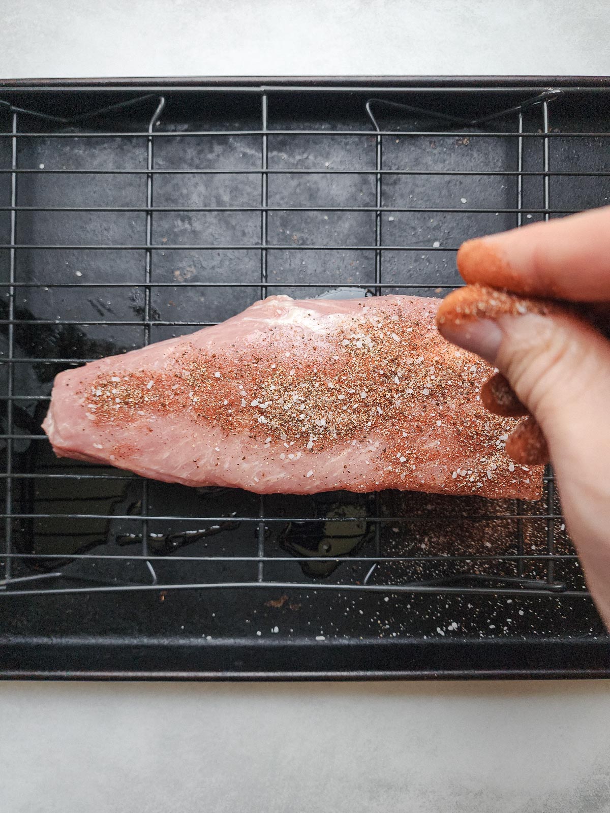 Sprinkling the coffee rub over the pork tenderloin.