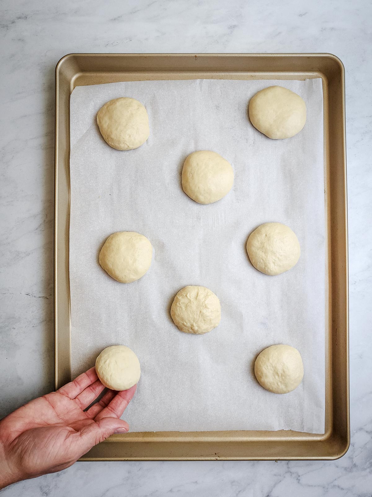 Ultimate Homemade Hamburger Buns Step 8: Flatten the balls into disks and stagger them on a parchment-paper lined baking sheet. Spacing them in a line allows the buns to touch while baking and causes them not to brown all the way around the edges.