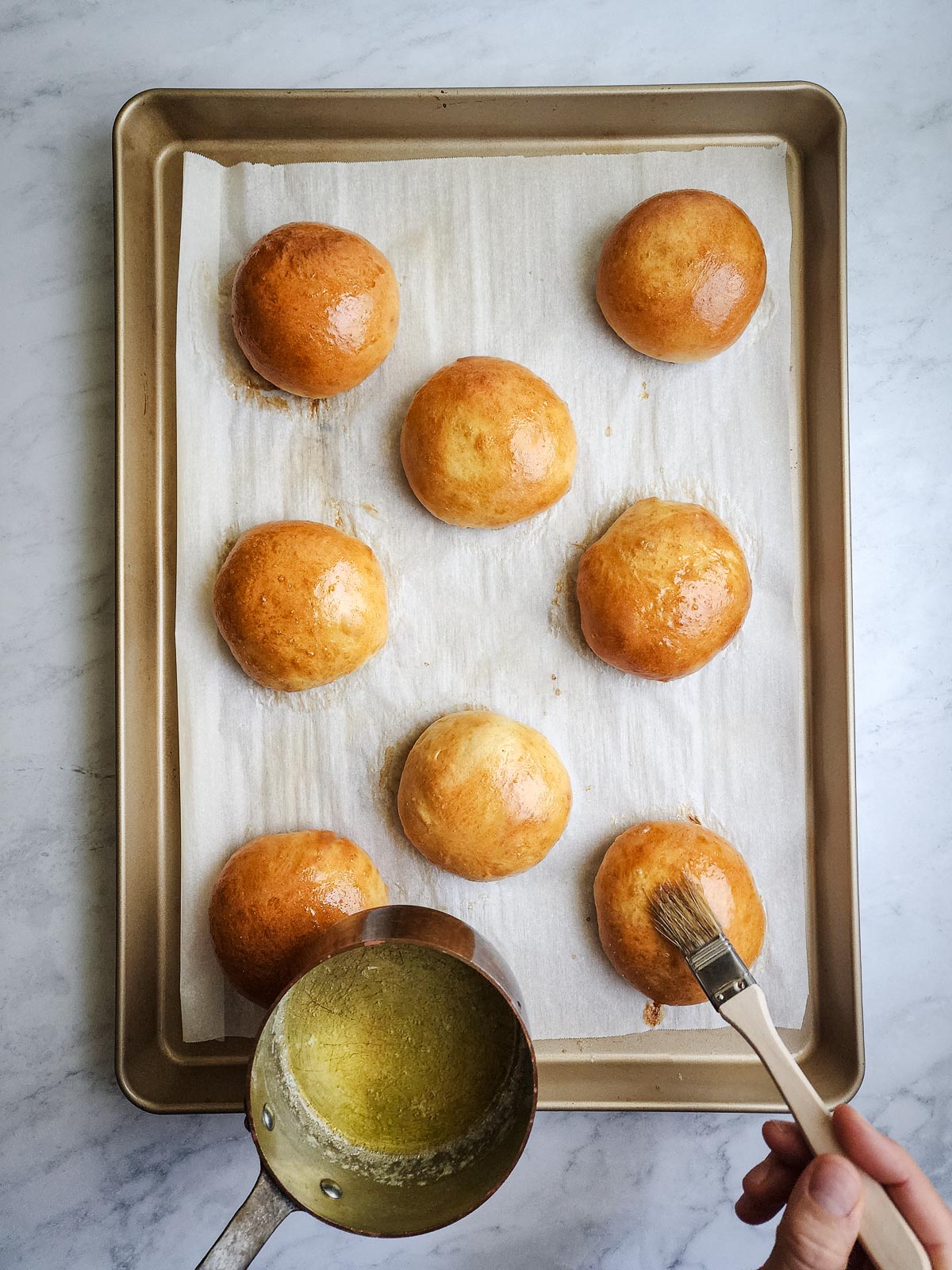 Brushing the Ultimate homemade hamburger buns with butter after baking.