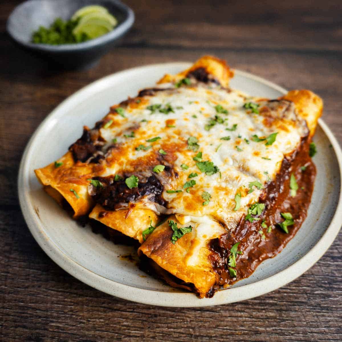 A plate of homemade chicken thigh enchiladas on a plate on a wooden table.