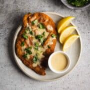 A white plate with chicken schnitzel topped with lemon cream sauce and fresh parsley.