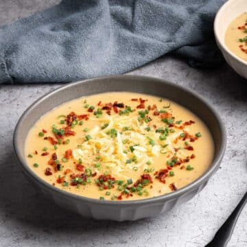 A bowl of potato leek soup garnished with crispy bacon, shredded Gouda, and fresh chives.
