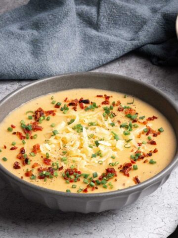A bowl of potato leek soup garnished with crispy bacon, shredded Gouda, and fresh chives.