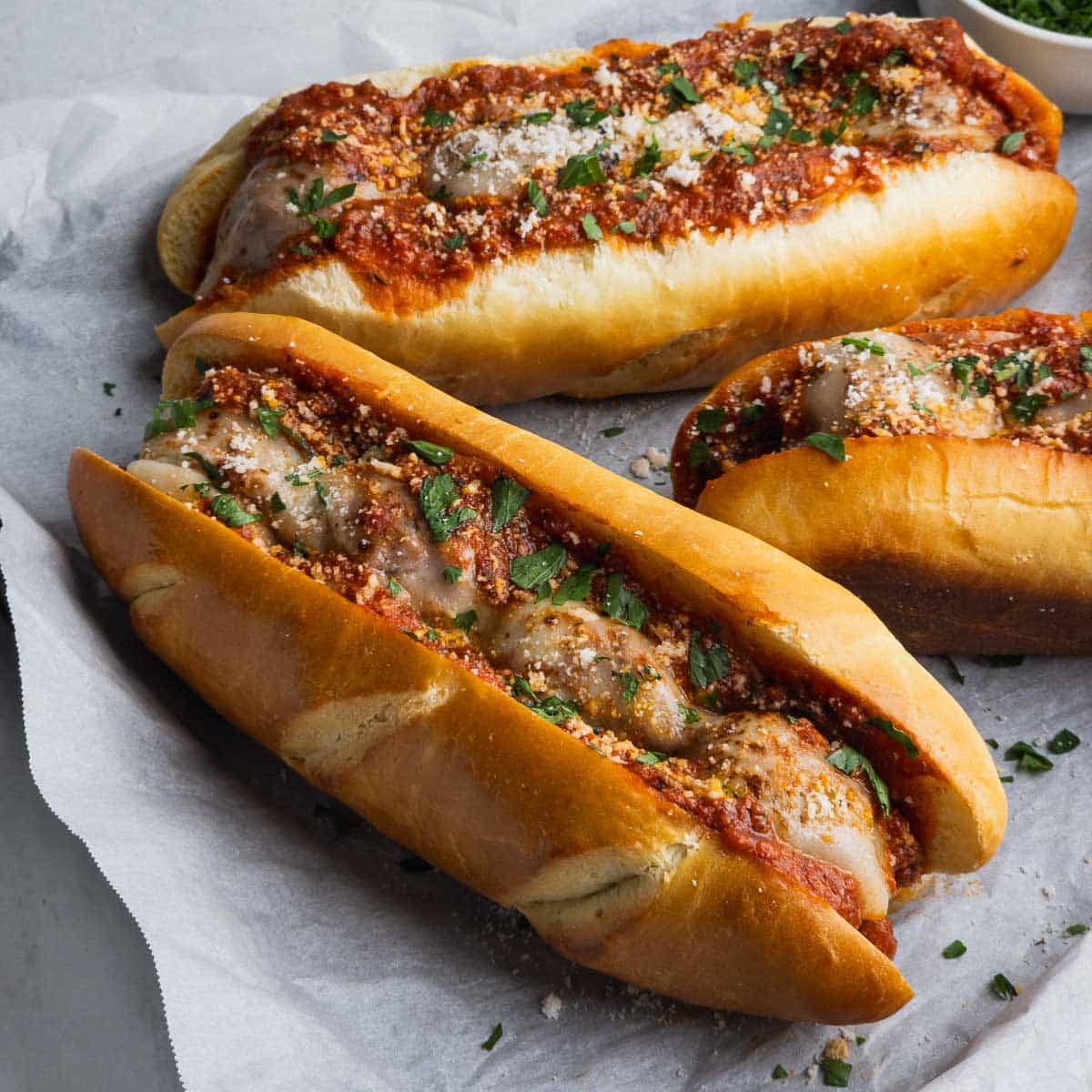 Baked meatball sub sandwiches garnished with grated Romano cheese on a parchment paper lined tray.