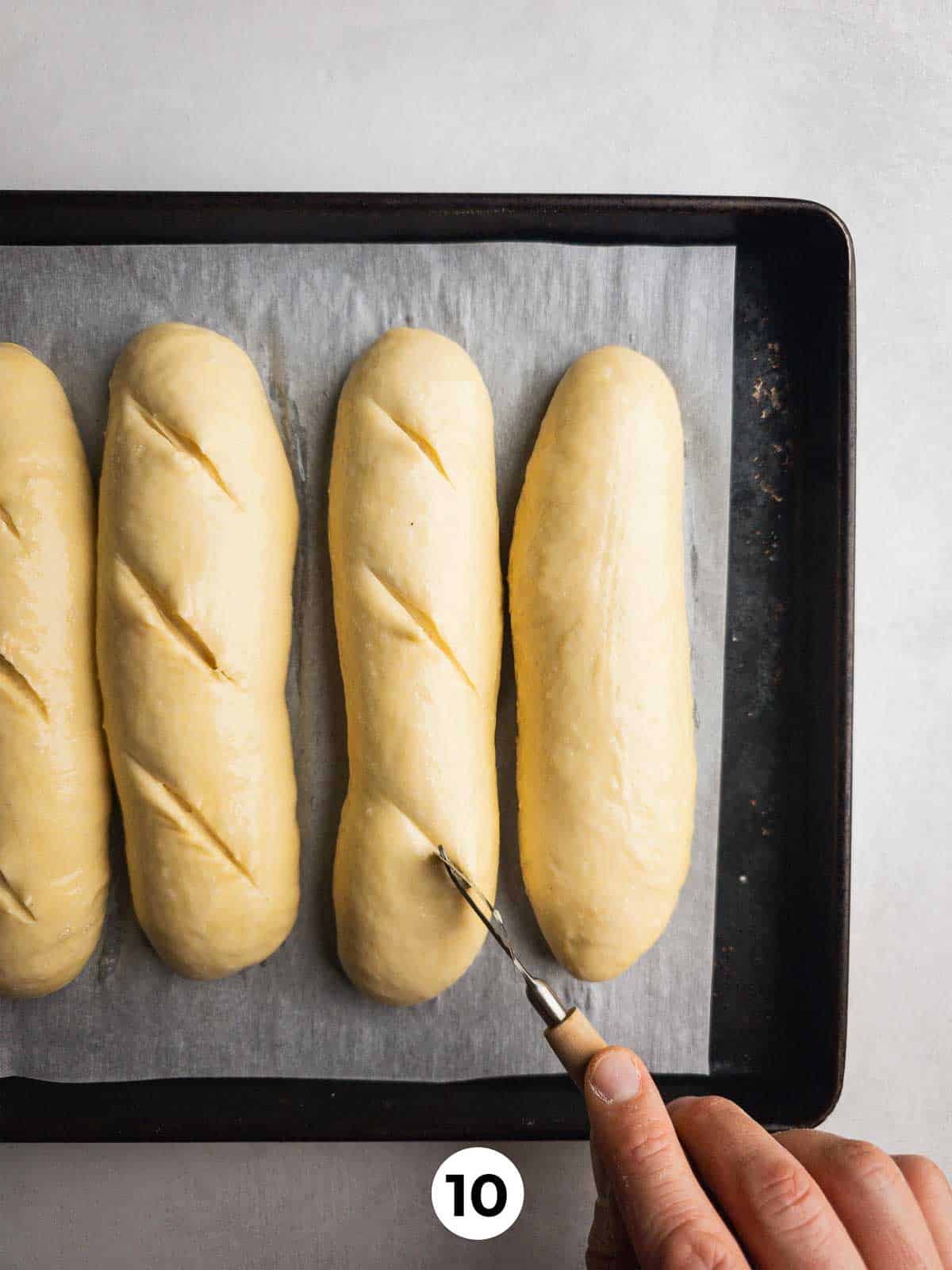 Scoring proofed sub rolls with a lame before baking.