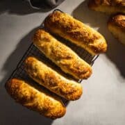 Italian Herb and Cheese Bread for sub rolls cooling on a wire rack on a marble counter.