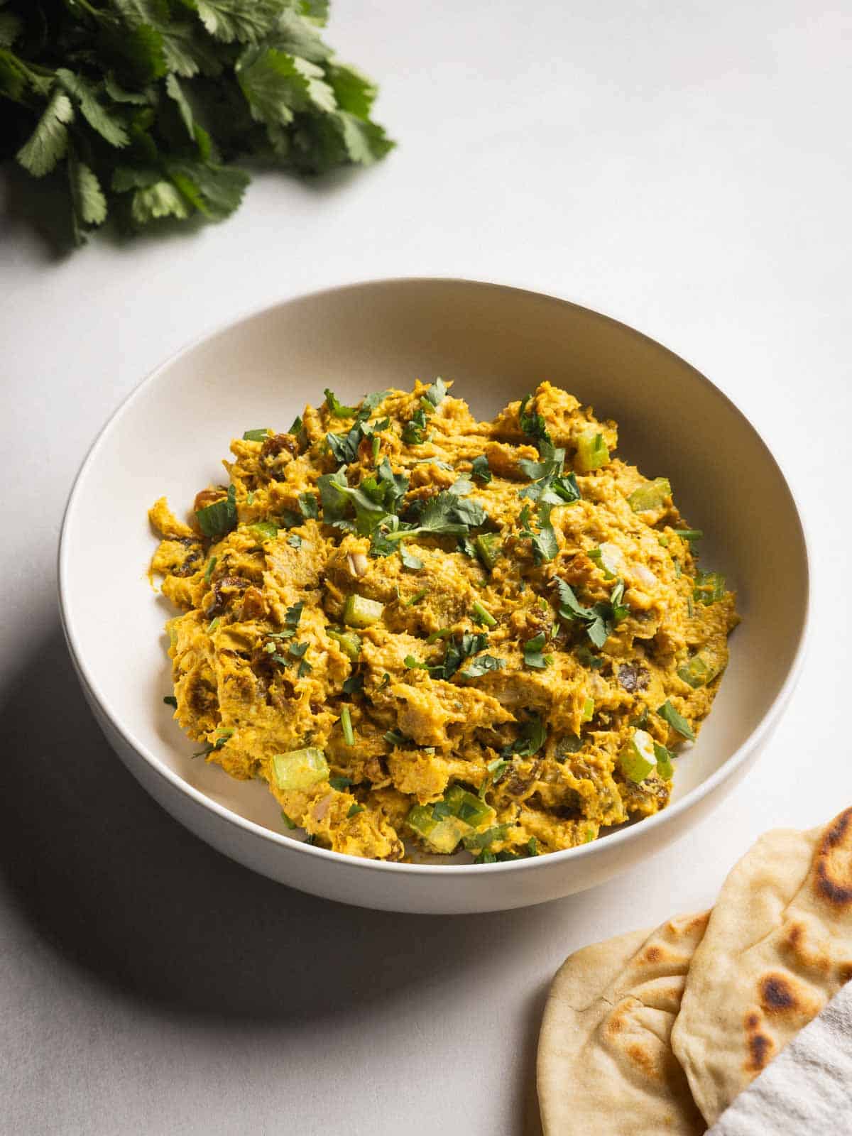 A bowl of curry chicken salad with rotisserie chicken served with naan and cilantro on the side.