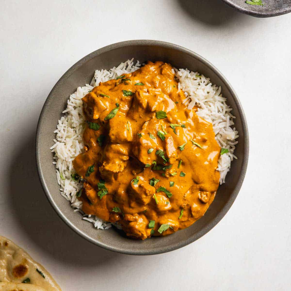 A bowl of easy butter chicken served over rice, garnished with cilantro, and served with naan bread.