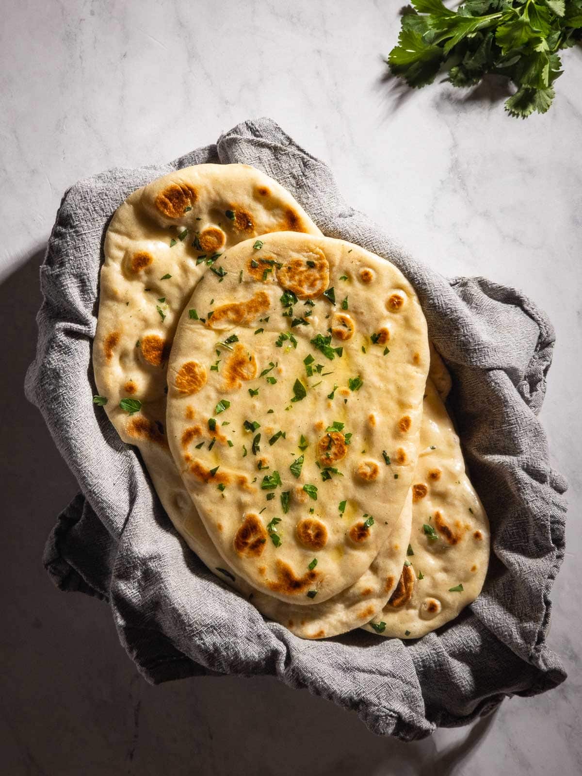 A basket of fresh-baked garlic naan bread brushed with herb butter.