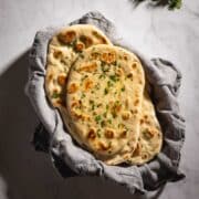 A basket of fresh-baked garlic naan bread brushed with herb butter.