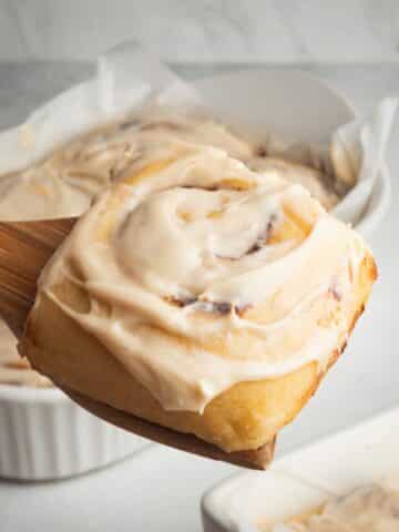 A cinnamon roll with cream cheese frosting being served.