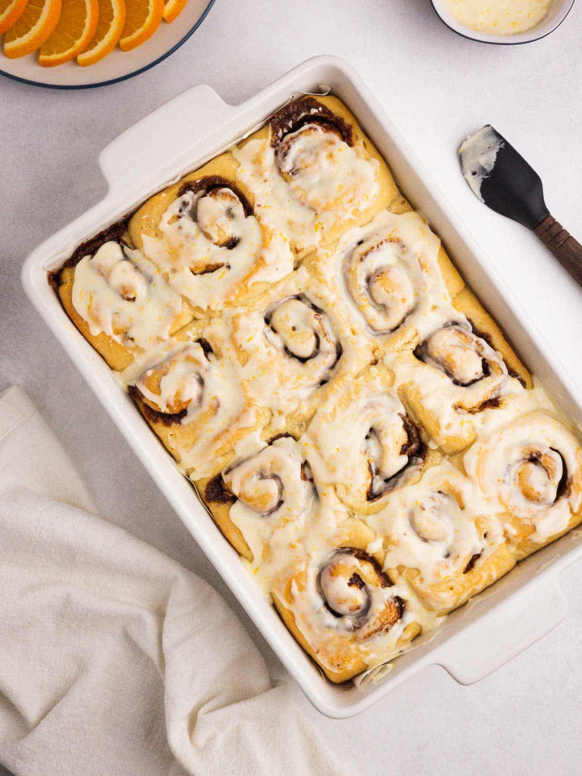 A tray of freshly baked orange cinnamon rolls topped with fresh orange glaze.