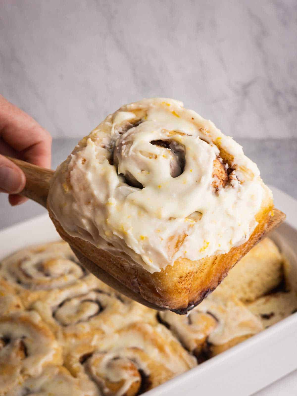 An orange glazed cinnamon roll being served.