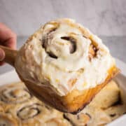 An orange glazed cinnamon roll being served.