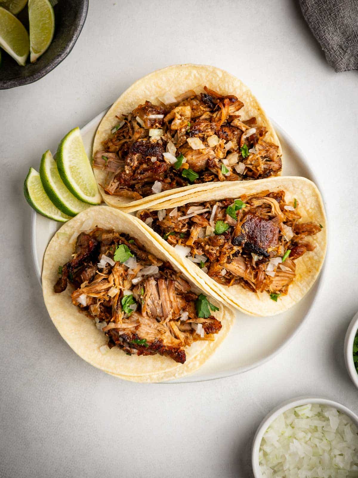 A plate of crispy carnitas street tacos topped with onions, cilantro, and lime juice.