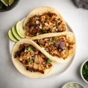 Crispy Carnitas Street Tacos served on a plate with onions, cilantro, and lime.