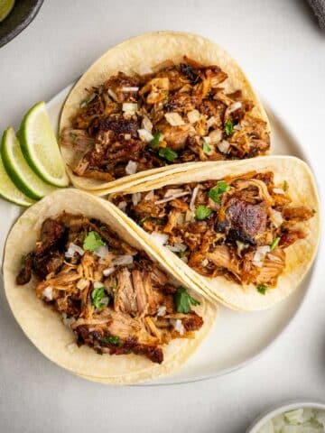 Crispy Carnitas Street Tacos served on a plate with onions, cilantro, and lime.