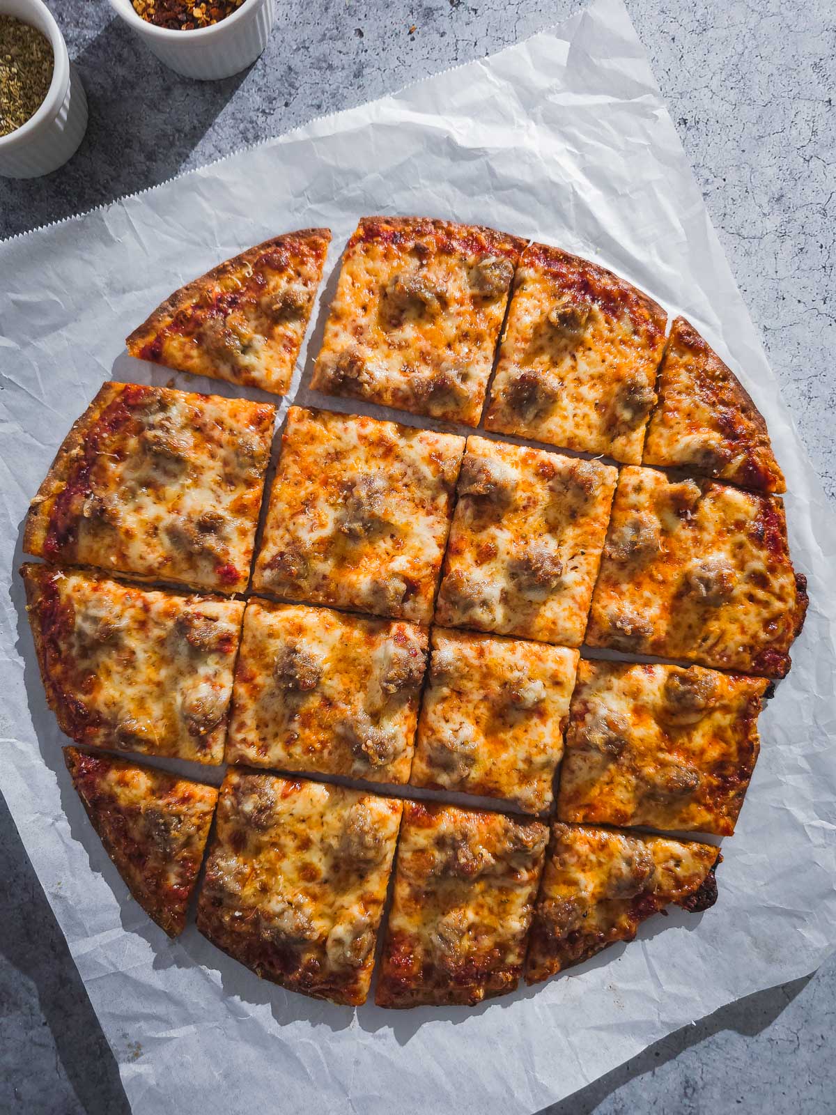Chicago Thin Crust Pizza with sausage, cut into squares, on parchment paper.