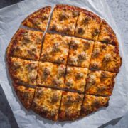 Chicago Thin Crust Pizza with sausage cut into squares on a piece of parchment paper.