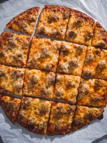 Chicago Thin Crust Pizza with sausage cut into squares on a piece of parchment paper.