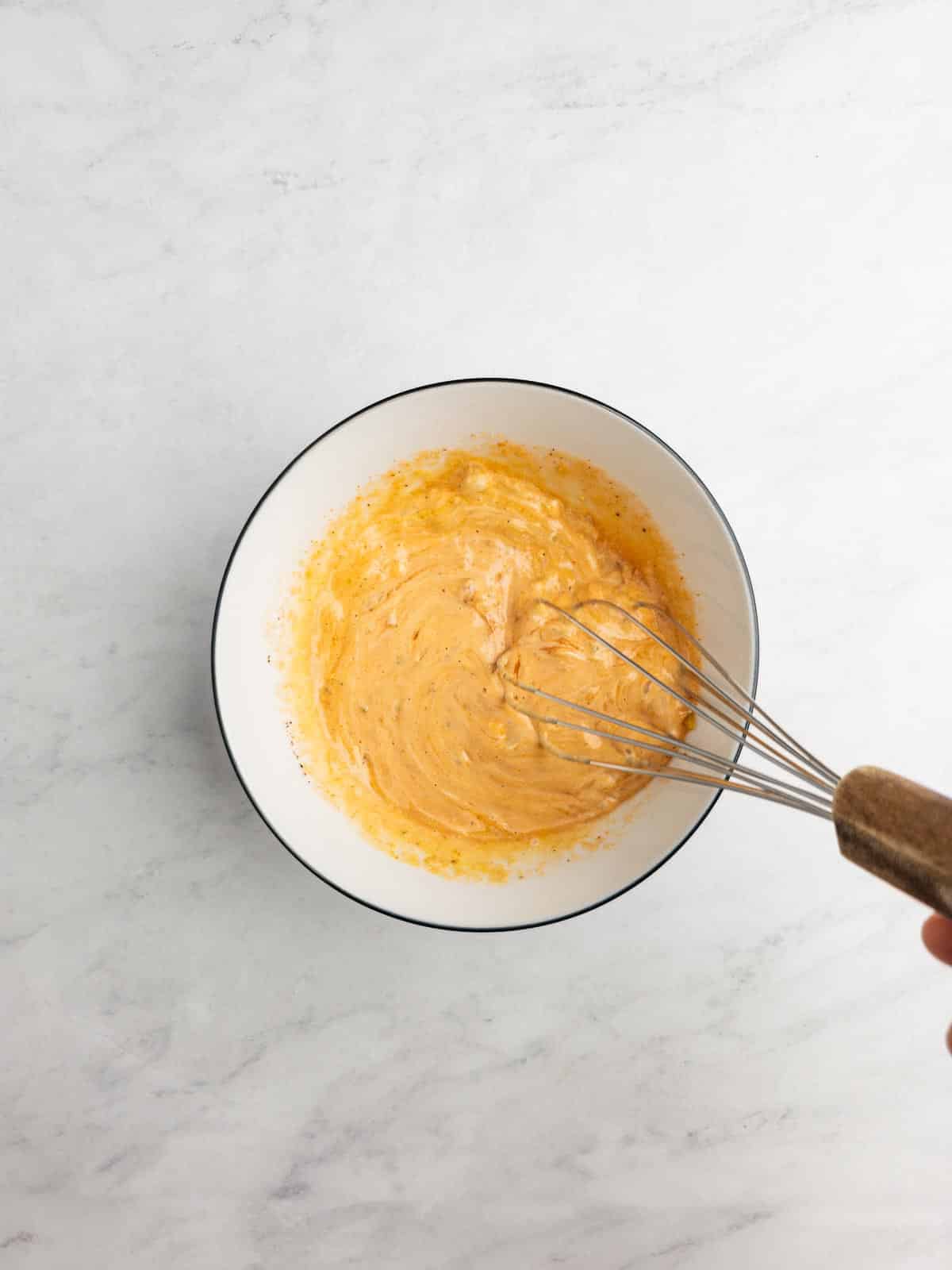 A whisk stirring ingredients for burger sauce together in a bowl.