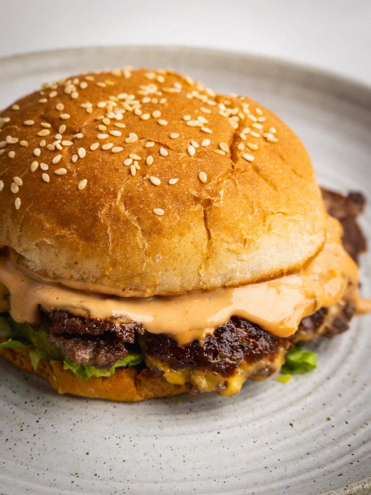 A smash burger on a plate with burger sauce dripping off the top patty.
