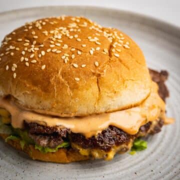 A smash burger on a plate with burger sauce dripping off the top patty.